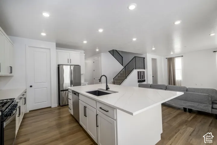 Kitchen island featuring a white surface, undermount rectangular sink, and matte black faucet, surrounded by white cabinetry, stainless steel appliances, recessed lighting, and wood-finish flooring