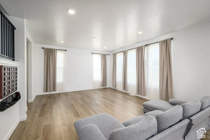 Living area featuring wood-finish flooring, recessed lighting, and multiple windows with curtain rod hardware