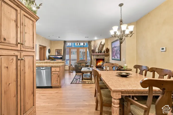 Natural wood-finish cabinetry, stone fireplace with a timber mantel, stainless steel dishwasher, wood-finish flooring, and multi-light chandelier