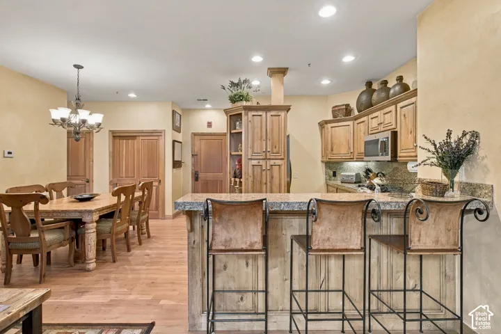 Kitchen featuring a breakfast bar, stone-finish countertops, custom wood cabinetry, wood-finish flooring, and recessed ceiling lighting