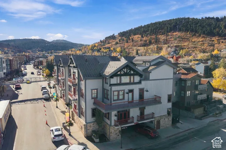 Multi-story building with metal roofing, vertical siding, stone masonry base, multiple external balconies, and covered off-street parking