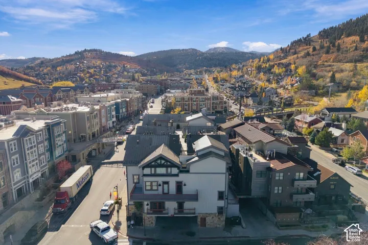 Aerial perspective of a multi-story building featuring stone-base exterior cladding, metal roofing, multiple private balconies, and proximity to mountain terrain