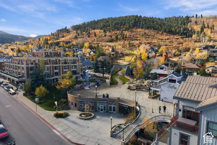 Aerial perspective of a multi-level complex featuring brick and siding exteriors, metal roofing, paved pedestrian plazas, integrated staircases, and a hillside mountain backdrop