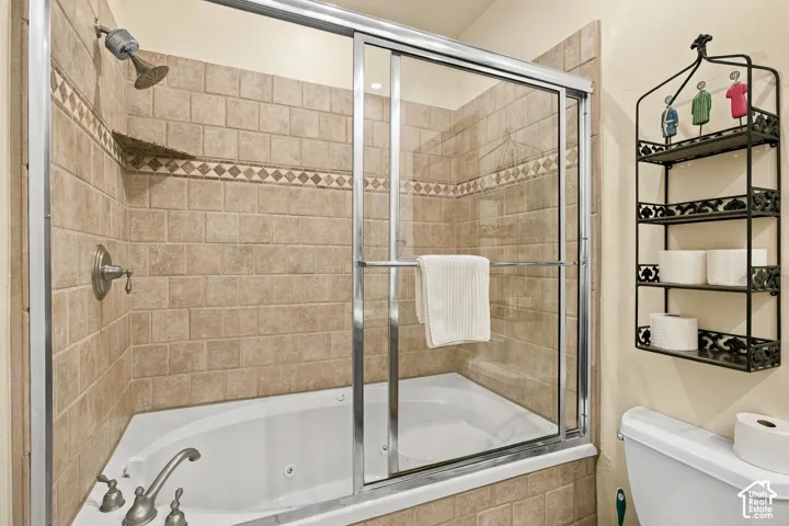 Jetted bathtub featuring a chrome-finish faucet set and sliding glass enclosure, surrounded by a ceramic tile wall with a decorative mosaic accent band