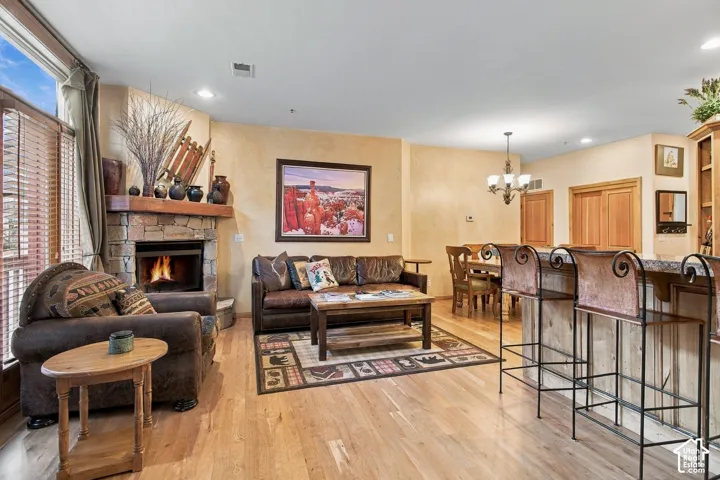 Open-concept living space featuring wood-finish flooring, stone fireplace with a timber mantel, recessed lighting, and a kitchen island with built-in cabinetry