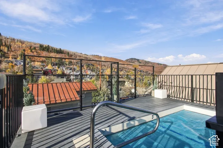 Rooftop deck featuring a composite wood-finish surface, recessed soaking pool with a stainless steel handrail, and a black metal railing with glass inserts