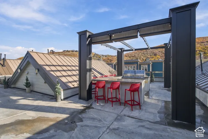 Rooftop terrace featuring a built-in outdoor kitchen with a stone countertop and stainless steel grill, sheltered by a custom dark-finish pergola