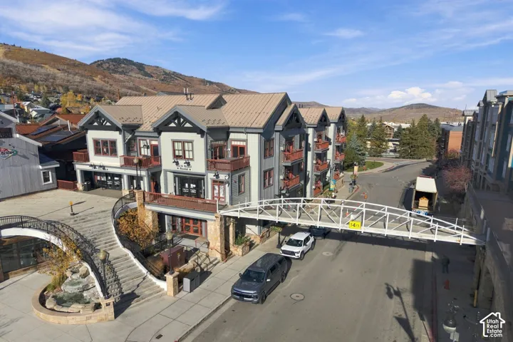 Multi-story complex featuring a metal roof, stone-clad foundation, exterior balconies, and a pedestrian skybridge