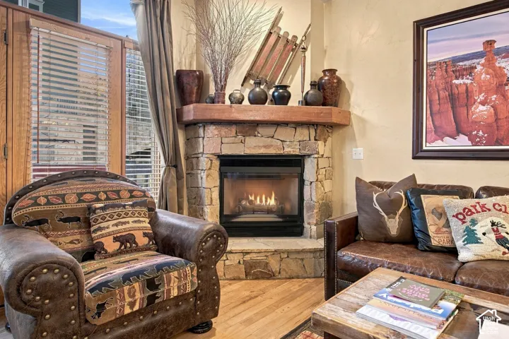 Corner fireplace featuring natural stone masonry, a heavy timber mantel, a glass-front insert, and a stone hearth, accented by wood-finish flooring