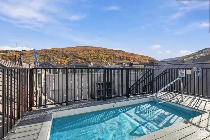 Rooftop hot tub with a tile-lined basin, metal handrail, mountain backdrop, and black metal perimeter fencing