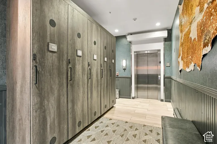 Floor-to-ceiling wood-finish storage lockers, stainless steel elevator, recessed lighting, tile flooring, and vertical wall paneling