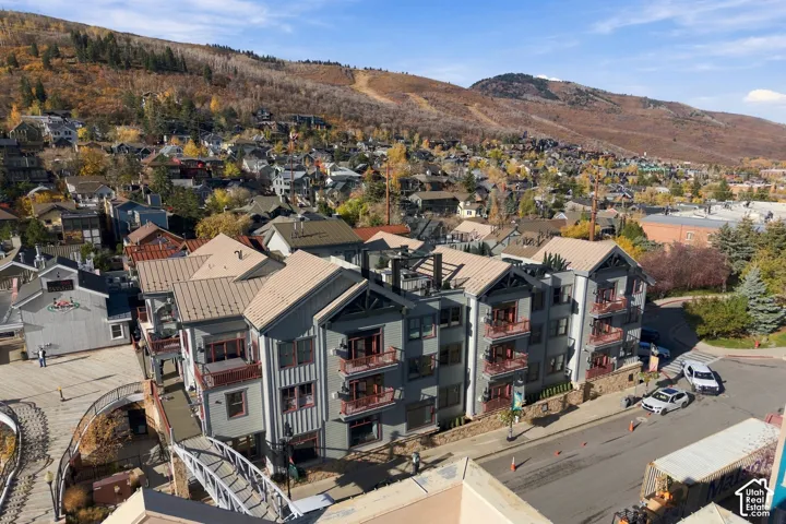 Multi-story building featuring board-and-batten siding, metal roofing, multiple private balconies, and stone masonry elements set against a mountainous backdrop