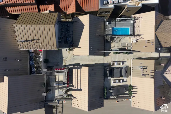 Aerial perspective of the property featuring a metal roofing system, an elevated swimming pool, a stone-finished outdoor kitchen structure, and paved ground-level hardscaping