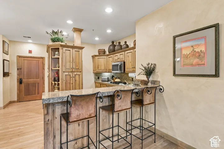 Kitchen featuring stained wood cabinetry, stone countertops, breakfast bar, recessed lighting, and wood-finish flooring