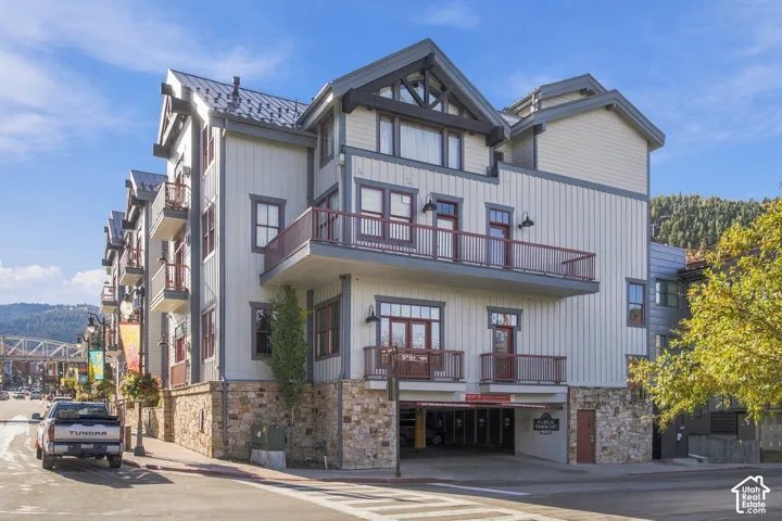Multi-story exterior featuring board-and-batten siding, natural stone veneer foundation, metal roof accents, and elevated steel-railed balconies