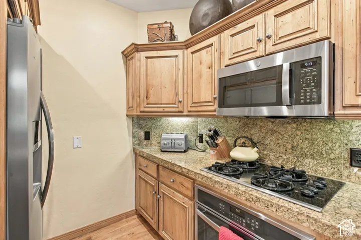 Kitchen featuring natural wood cabinetry, stone-surface countertops, stone tile backsplash, stainless steel gas cooktop, and built-in stainless steel microwave