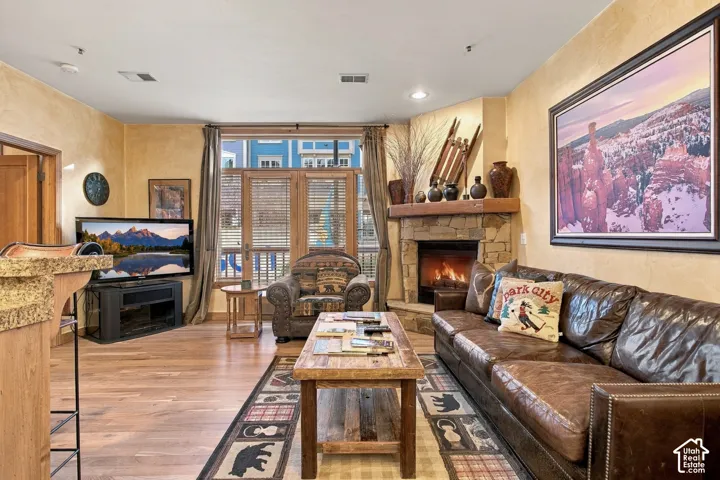 Living area featuring a floor-to-ceiling stone-faced fireplace with a wood mantel, wood-finish flooring, and expansive windows with glass-paned doors