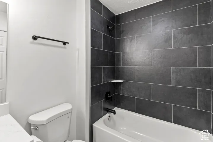 Bathroom featuring a deep soaking tub with a matte black shower fixture, dark rectangular wall tile, built-in corner shelving, and a matte black towel bar