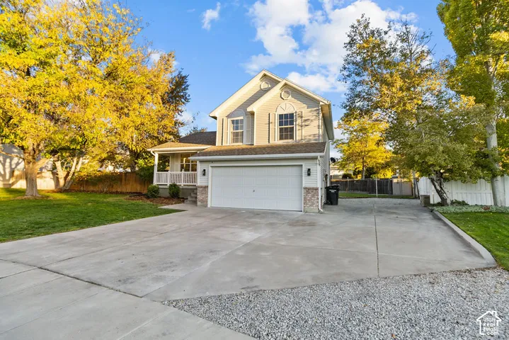 Two-story residence featuring light-toned horizontal siding, stone veneer accents, a covered front porch with white railing, and an attached two-car garage