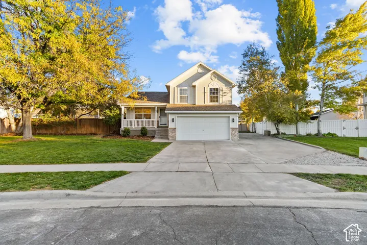Two-story residence featuring a covered front porch, stone-accented facade, attached multi-car garage, concrete driveway, and mature landscaping