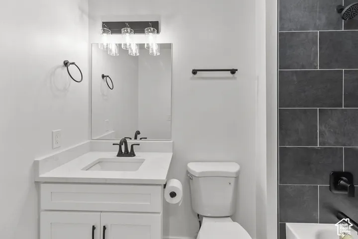 Bathroom featuring a white vanity with a rectangular sink, stone-finish countertop, matte black fixtures, and a shower surround tiled in large-format charcoal stone