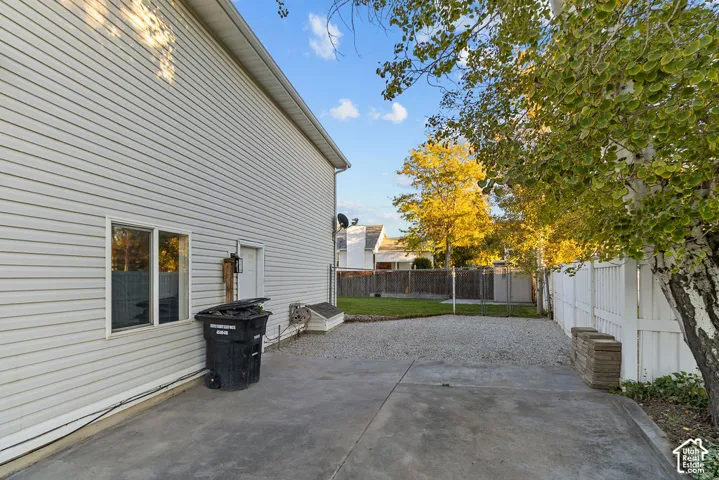 Exterior side yard featuring horizontal vinyl siding, concrete paving, a gravel surface, and a vinyl privacy fence