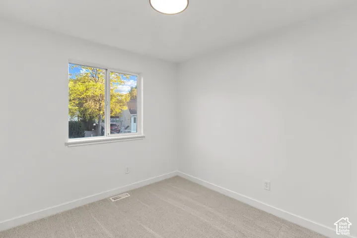 Room featuring neutral wall tones, carpeted flooring, a sliding window with exterior greenery, and a flush-mount ceiling light