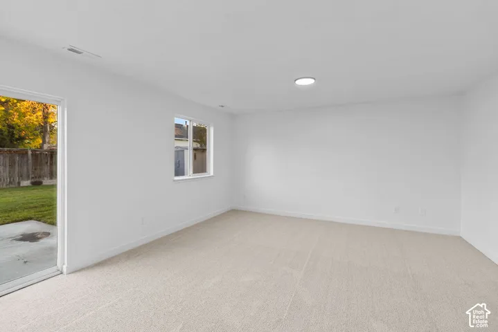 Interior room featuring neutral wall-to-wall carpeting, white walls, flush-mount ceiling lighting, and a sliding glass door providing exterior access