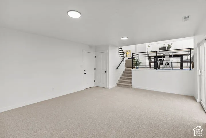 Neutral-toned wall-to-wall carpeting, modern recessed ceiling lighting, and a metal horizontal-bar stair railing