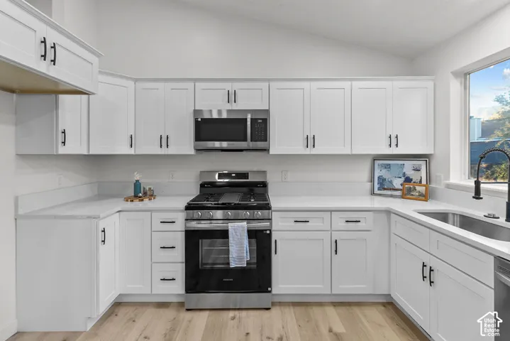 Kitchen featuring white shaker-style cabinetry, solid-surface countertops, stainless steel appliances, a vaulted ceiling, and wood-finish flooring