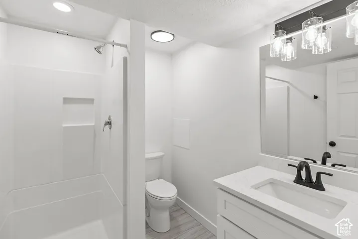 Bathroom featuring a white vanity with a quartz countertop, matte black faucet, wall-mounted vanity lighting, and a composite shower surround