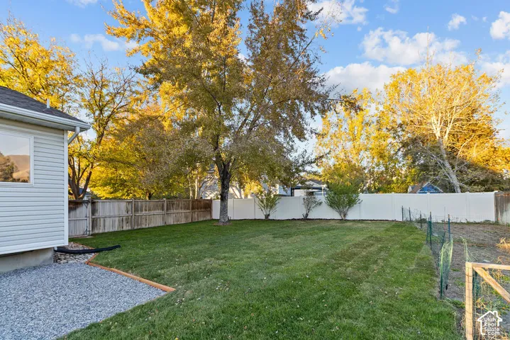 Backyard featuring a manicured lawn, white vinyl fencing, wood-slat perimeter fencing, and a gravel patio area