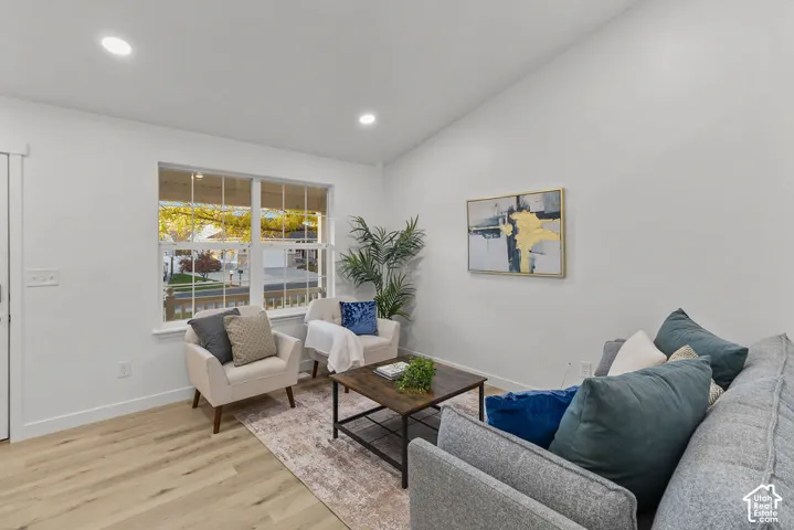 Vaulted ceiling with recessed lighting, wide-plank wood-finish flooring, and a multi-pane window