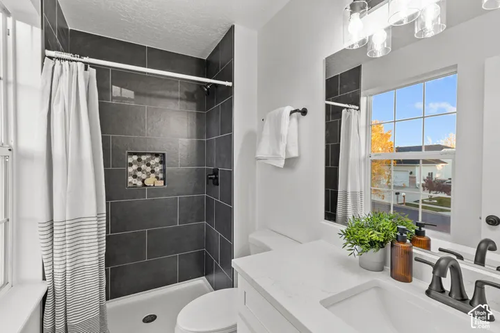 Bathroom featuring dark tile shower surround with integrated mosaic niche, white quartz vanity countertop, matte black hardware, and multi-light fixture
