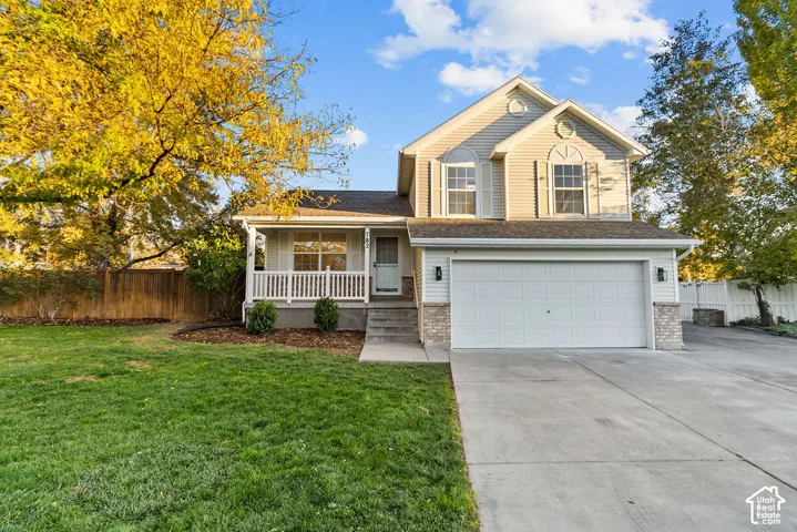 Two-story residence featuring light-toned vinyl siding, stone masonry accents, a covered front porch with white railing, and an attached two-car garage