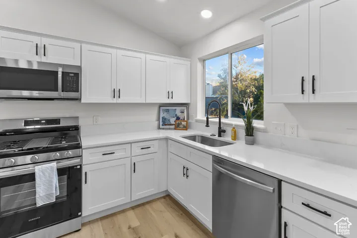 Kitchen featuring white shaker-style cabinetry, quartz countertops, stainless steel appliances, matte black hardware, and wood-finish flooring