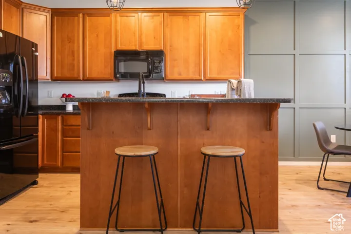 Kitchen featuring wood cabinetry, an island with stone-finish countertops, black built-in appliances, wood-finish flooring, and a paneled accent wall