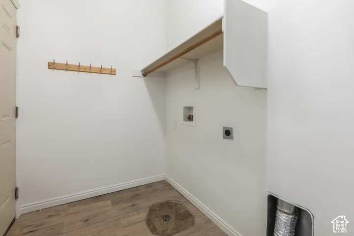 Utility area featuring wood-finish flooring, a wall-mounted hook rack, an overhead storage shelf, and recessed water and dryer vent hookups