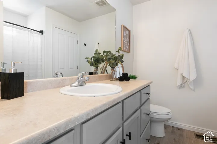 Bathroom featuring a light-toned countertop, grey cabinetry with matte black hardware, an integrated sink with a chrome faucet, full-width mirror, and wood-finish flooring