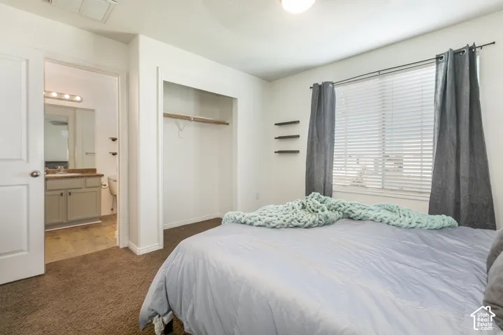 Bedroom featuring carpeting, window with horizontal blinds, built-in closet with shelving, and entry to a bathroom equipped with a vanity, countertop, and mirror