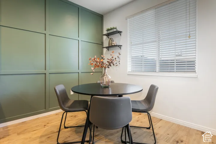 Room featuring an accent wall with square millwork molding, wood-finish flooring, and horizontal window blinds with two mounted wall shelves