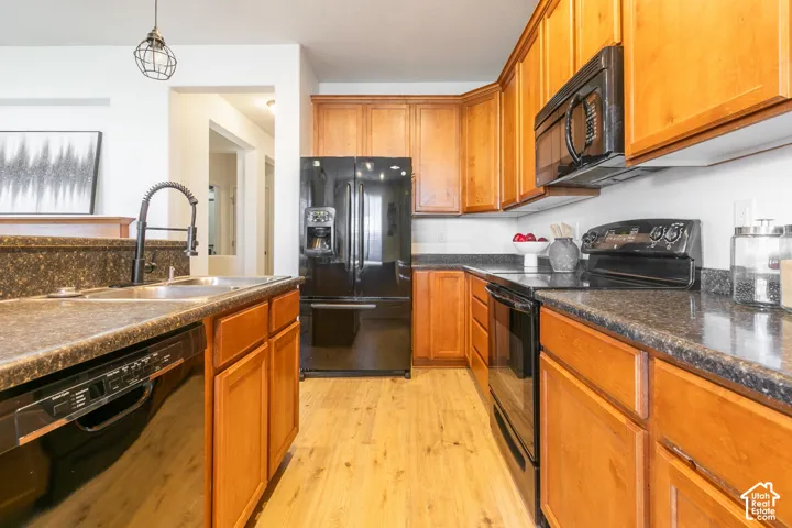 Kitchen featuring wood cabinetry, dark stone-finish countertops, black built-in appliances, wood-finish flooring, and a gooseneck faucet