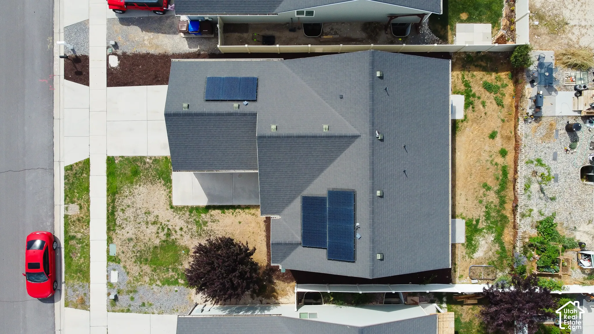 Aerial view of residential property featuring a composition shingle roof, roof-mounted solar panels, a paved driveway, and side yard