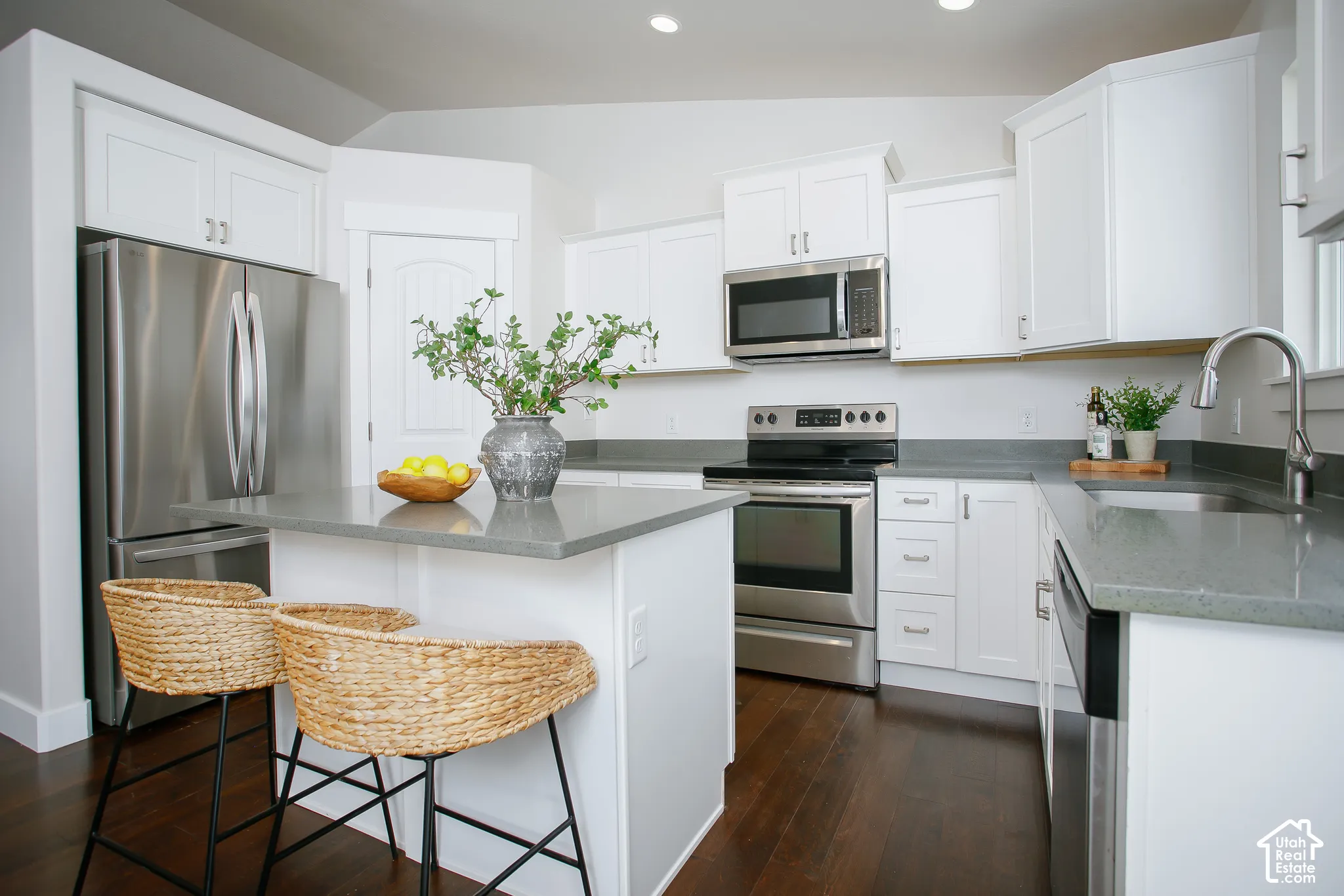 Kitchen featuring white cabinetry, solid-surface countertops, wood-finish flooring, an integrated island, and stainless steel appliances