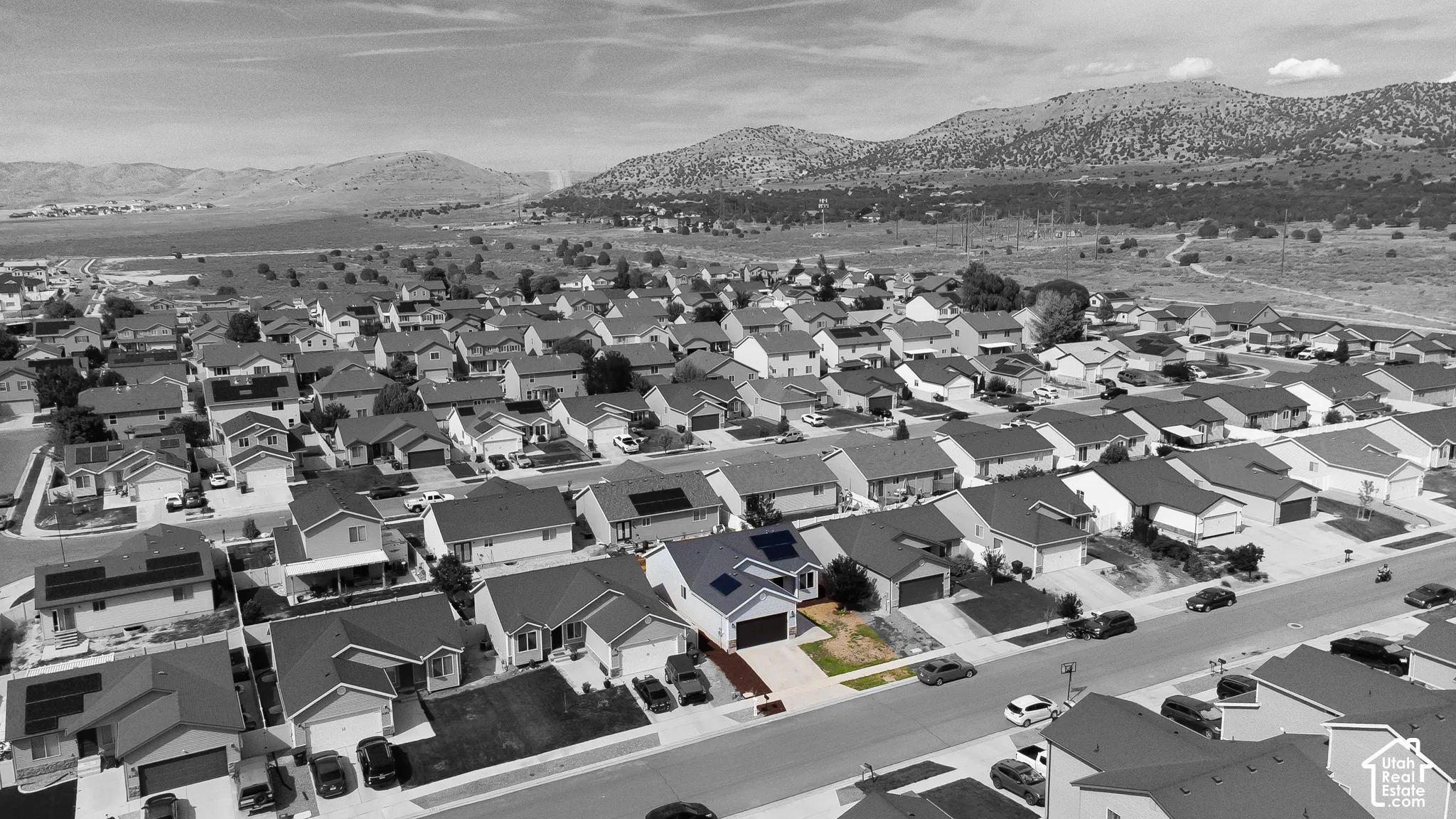 Aerial perspective featuring a single-family residence with roof-mounted solar panels, an attached two-car garage, and a concrete driveway, set against a mountainous landscape