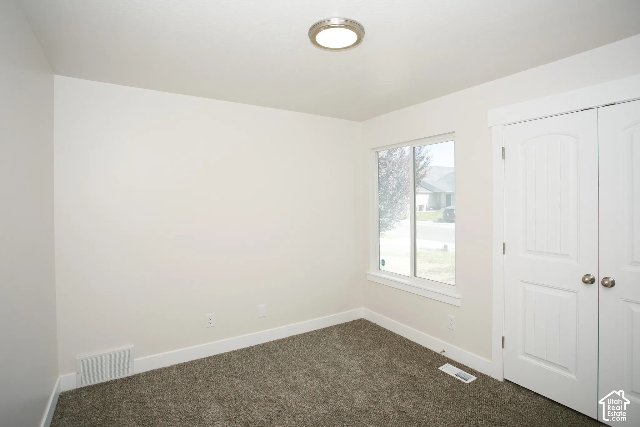 Neutral wall paint, carpeting, double-panel closet doors, and a flush-mount ceiling light fixture