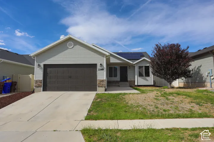 Single-story residence featuring light-colored horizontal siding, stone veneer accents, a dark-toned two-car garage door, and roof-mounted solar panels
