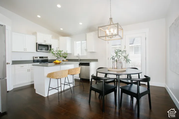 Kitchen featuring white cabinetry, solid-surface countertops, stainless steel appliances, wood-finish flooring, and a geometric chandelier