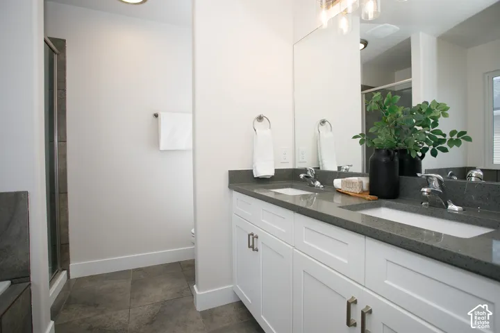Dual-sink vanity with stone countertop, white shaker-style cabinetry, large wall-mounted mirror, brushed metal fixtures, and tile flooring