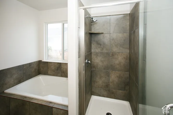 Bathroom featuring a drop-in soaking tub with a tiled surround, a glass-enclosed shower with a built-in tiled corner shelf, and neutral-tone square wall tile